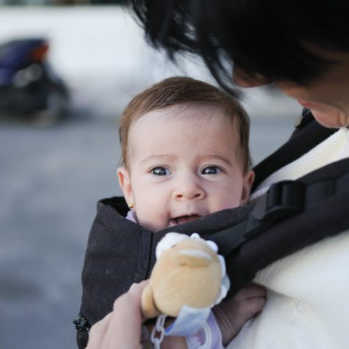 Mother carrying her baby girl in a baby carrier Mother carrying her baby girl in a baby carrier outdoors